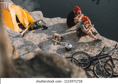 High Angle View Of Active Bike Travellers Eating Canned Food In Camping On Rocky Cliff