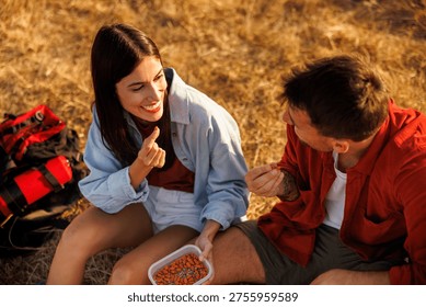 High angle view of active couple taking a hiking break, sitting on the grass relaxing and having a heathy snack