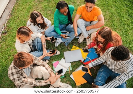 High angle view or aerial of a group of students sitting on a circle at the university campus lawn. Classmates resting outside of the highschool, talking together. Teenage friends using smart phones