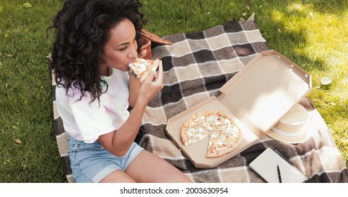 high angle view of african american woman eating pizza during picnic in park - Powered by Shutterstock