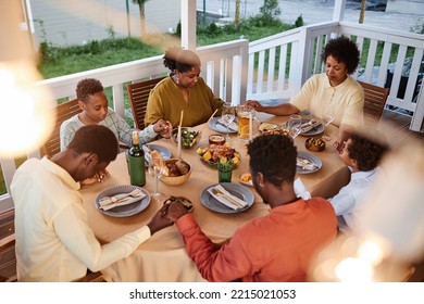 High angle view of African American family saying grace at dinner table outdoors and holding hands in cozy evening setting - Powered by Shutterstock