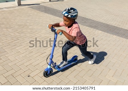 High angle view of african american boy riding push scooter on promenade during sunny day. unaltered, childhood, and learning concept.