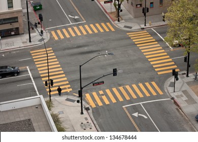 A high angle view of an almost empty street intersection, with yellow cross walk markings, traffic signal lights, and curb cuts, in San Jose, California.