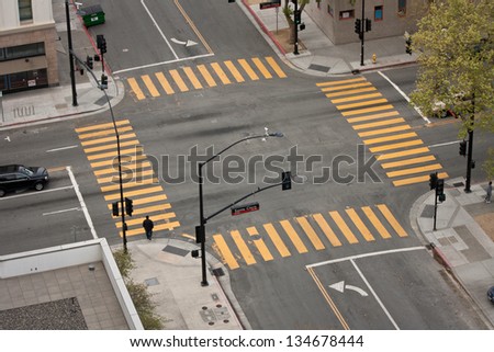 A high angle view of an almost empty street intersection, with yellow cross walk markings, traffic signal lights, and curb cuts, in San Jose, California.
