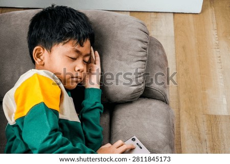 High Angle View of an Asian Boy Sleeping on Sofa with His Hand Touching Smartphone