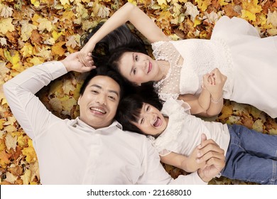 High Angle View Of Asian Family Lying On Autumn Leaves, Shot Outdoors