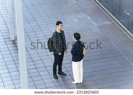 High angle view of Asian male and female business people having a conversation in front of an office building.