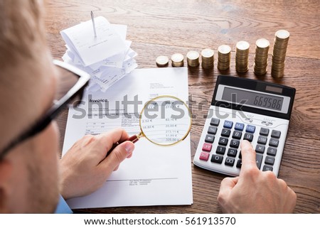 High Angle View Of A Auditor Hand Calculating Invoice Using Calculator On Desk. Tax Scrutiny And Fraud Investigation Concept