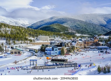 High Angle View Of Base Ski Village In Colorado, USA, Ski Resort On Nice Winter Day; Mountain Range And Sky In Background