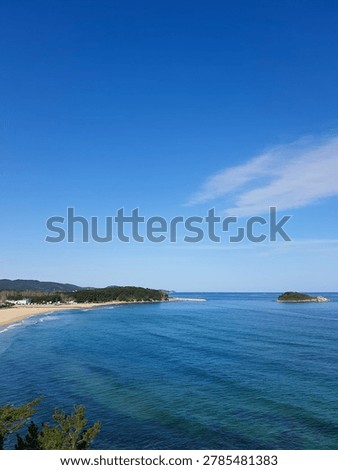 High angle view of beautiful blue sea with a sand beach, faraway red lighthouse, and a small island under clear blue sky. Copy space for text.