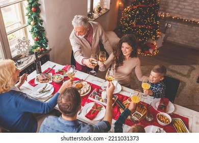 High angle view of a beautiful happy family gathered around the table, having Christmas dinner all together at home, celebrating Christmas and making a toast - Powered by Shutterstock