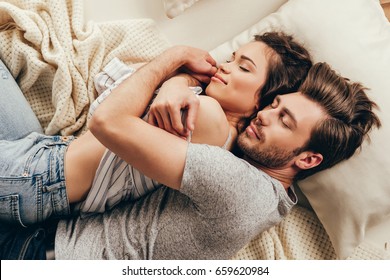 High angle view of beautiful happy young couple hugging while sleeping on bed