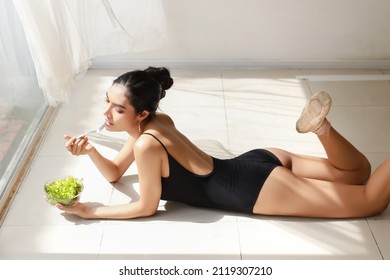 high angle view beautiful healthy and sporty asian young woman holding salad bowl and eat after training ballet dancing while lying down