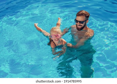Schöne Aussicht auf das schöne kleine Mädchen und ihren Vater, die sich an einem sonnigen Sommertag im Schwimmbad amüsieren, Vater lehrt Tochter schwimmen