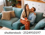 High angle view of beautiful young couple in love hugging and posting on social networks using smart phone while relaxing at home, woman sitting in man