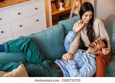 High angle view of beautiful young couple in love relaxing and cuddling at home, man lying with head in his wife's lap while she is hugging him and stroking his hair - Powered by Shutterstock