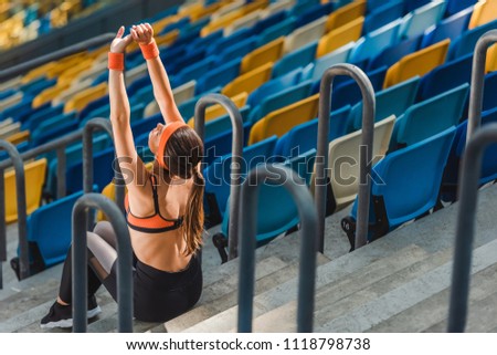 high angle view of beautiful young woman stretching up while sitting on stairs at sports stadium