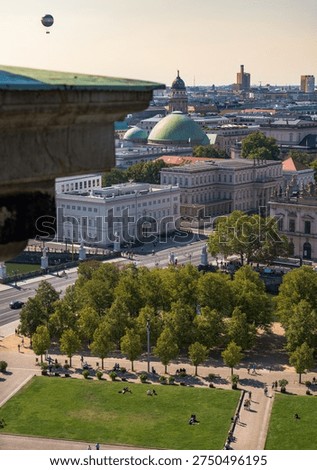 High angle view in Berlin shows Lustgarten lawns with people, Unter den Linden facades, St. Hedwig's Cathedral domes, Franzosischer Dom tower, and Die Welt balloon at left.