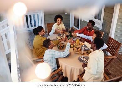 High angle view at big African American family clinking glasses over dinner table outdoors in cozy setting with fairy lights - Shutterstock ID 2215064885