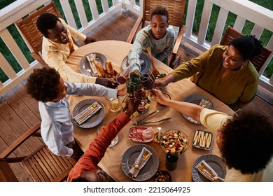 High Angle View At Big African American Family Clinking Glasses Over Dinner Table Outdoors In Cozy Evening Setting