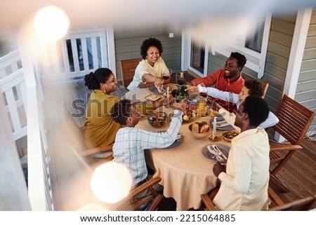 High angle view at big African American family clinking glasses over dinner table outdoors in cozy setting with fairy lights