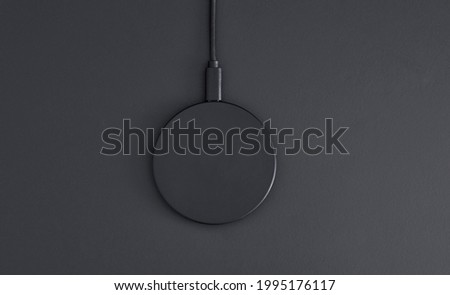 High angle view of black plastic circular wireless charger laying on dark grey desk. Modern technology, wireless device and transfer of energy concept.