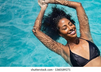 High Angle View Of Black Woman Relaxing In The Water With Closed Eyes. Portrait Of Happy Woman In Bikini Floating In A Water. Top View Of Relaxed African Girl In Swimming Pool With Copy Space.