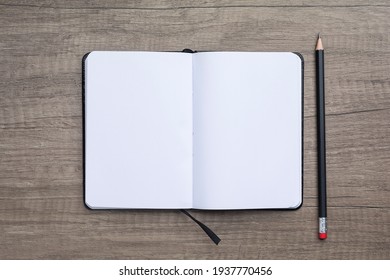 High angle view of blank opened note pad and black pencil on wooden background. 