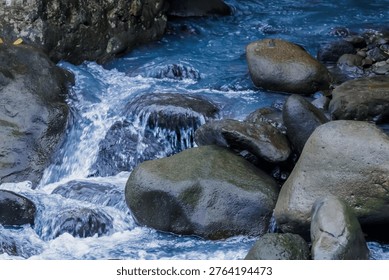 High angle view of a blue-tinted river flowing over smooth grey boulders, creating a serene and refreshing nature scene.