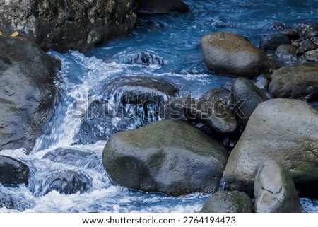 High angle view of a blue-tinted river flowing over smooth grey boulders, creating a serene and refreshing nature scene.