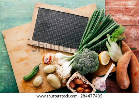 High Angle View of Bounty of Fresh Vegetables on Wooden Cutting Board with Black Board Marked with Grid Lines, Still Life on Rustic Wooden Background