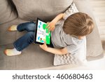 High Angle View Of Boy Sitting On Sofa Enjoying Game On Digital Tablet