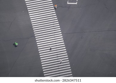 A high angle view of a broad striped crossing in a dense commercial district captures riders strung out in single file along the crossing. In the core of a busy business quarter.