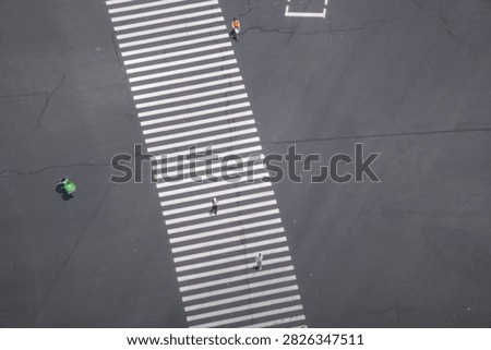 A high angle view of a broad striped crossing in a dense commercial district captures riders strung out in single file along the crossing. In the core of a busy business quarter.