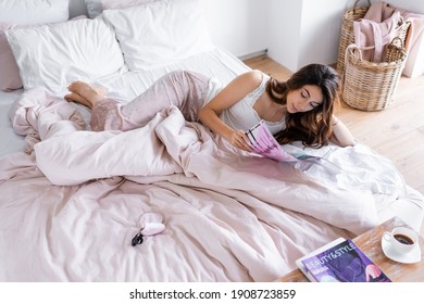 High Angle View Of Brunette Woman In Pajama Reading Magazine Near Coffee In Bedroom