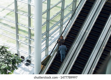 High Angle View Of Business People Interacting With Each Other While Moving Upstairs On Escalator In Office. Modern Corporate Start Up New Business Concept With Entrepreneur Working Hard