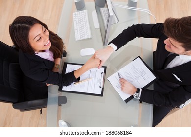 High Angle View Of Business People Shaking Hands At Desk In Office