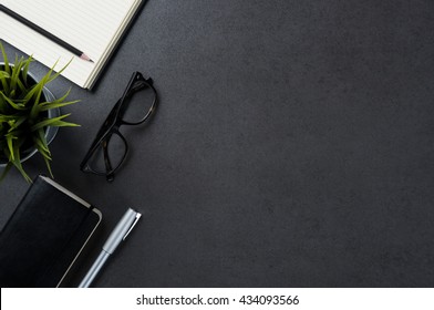High angle view of businessman desk with organizer, pen, glasses and green plant. Top view of office supplies on blackboard background with copy space.