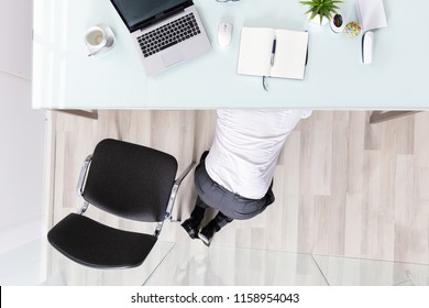 High Angle View Of A Businessman Hiding Under Desk In Office