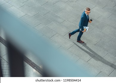 High Angle View Of Businessman With Paper Cup And Newspaper Walking On Street