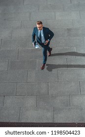 High Angle View Of Businessman With Paper Cup And Newspaper Walking On Street   