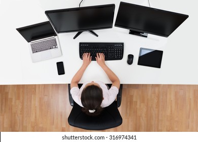 High Angle View Of Businesswoman With Multiple Computers At Desk