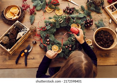 High angle view of busy woman standing at desk and using decorative ribbon while making Christmas wreath - Shutterstock ID 2172598401