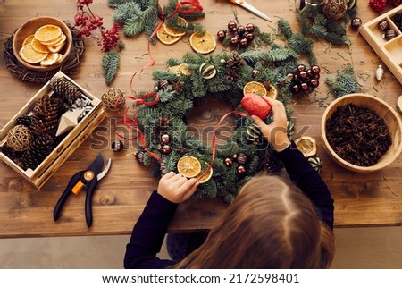 High angle view of busy woman standing at desk and using decorative ribbon while making Christmas wreath