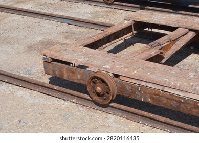 A high angle view captures an old weathered wooden slipway cradle cart with a rusty metal wheel resting on steel rail tracks at a shipyard
