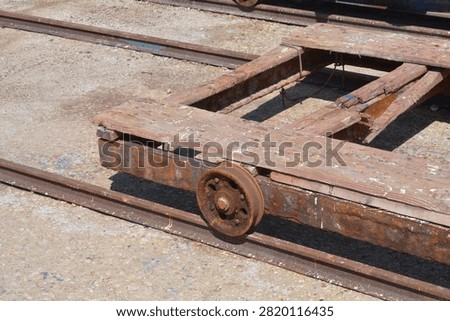A high angle view captures an old weathered wooden slipway cradle cart with a rusty metal wheel resting on steel rail tracks at a shipyard