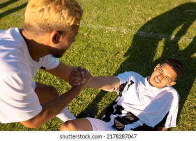 High angle view of caucasian player assisting injured teammate lying on field in getting up. Match, playground, summer, pain, unaltered, soccer, sport, teamwork, togetherness and competition. - Powered by Shutterstock