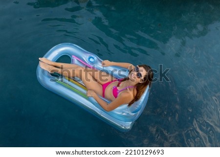 High angle view of a Caucasian woman wearing beachwear and sunglasses sitting on an inflatable pool lounger sunbathing in a swimming pool on a sunny day