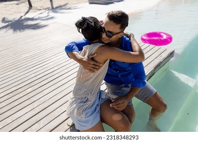 High angle view of caucasian young couple embracing while sitting at poolside at tourist resort. Copy space, unaltered, vacation, love, together, lifestyle, enjoyment, romance, beach and summer. - Powered by Shutterstock