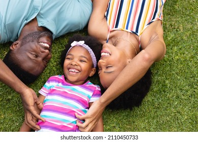 High angle view of cheerful african american parents lying with daughter on grass at garden. family, love and togetherness concept, unaltered.